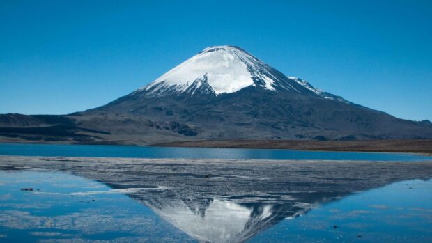 A snowcapped mountain is reflected in a calm lake under a clear blue sky in Bolivia, 2K Desktop Wallpaper