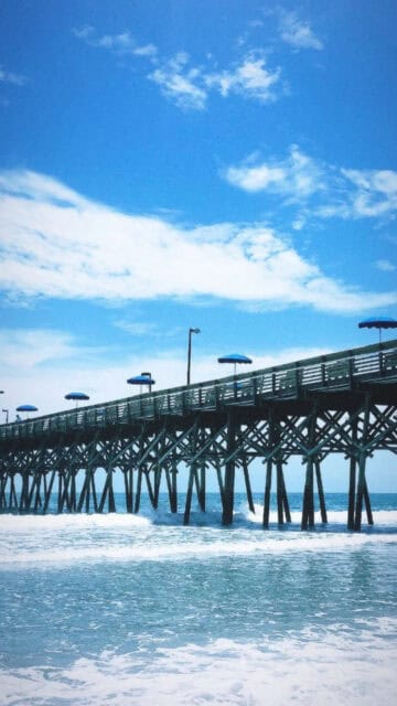 South Carolina Beach Pier with Blue Umbrellas and Clear Sky Wallpaper