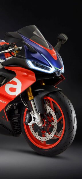 The Aprilia motorcycle features a sleek front design with illuminated headlights and sporty red and blue colors, HD Mobile Wallpaper