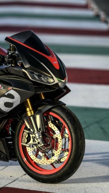 A close up of a sporty Aprilia motorcycle front wheel and headlight on a racetrack, HD Mobile Wallpaper