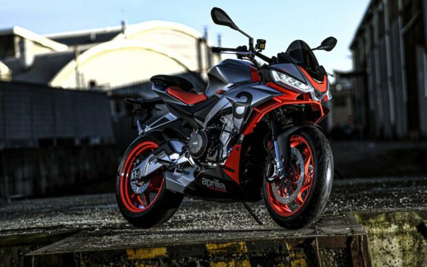 A sporty Aprilia motorcycle with red and black accents parked on an industrial platform, HD Desktop Wallpaper