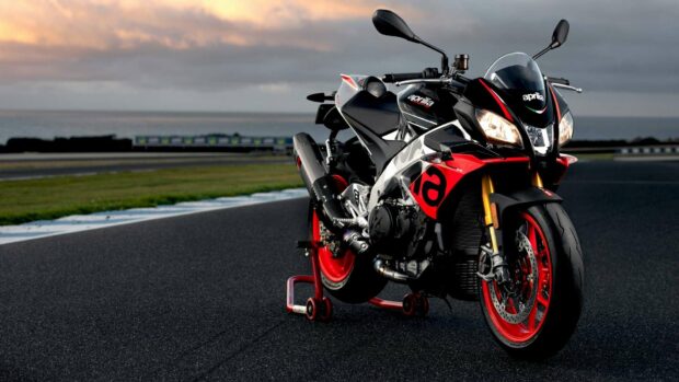 A sporty Aprilia motorcycle is parked on the racetrack at sunset with vibrant red accents on the wheels, HD Desktop Wallpaper