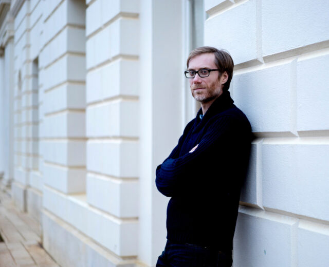 Stephen Merchant casual portrait leaning on white wall in urban setting wallpapers