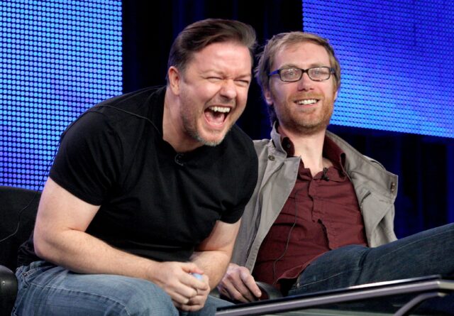 Stephen Merchant laughing with friend on stage in casual attire vibrant background wallpaper
