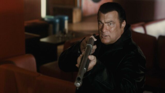 Steven Seagal Intense Action Pose with Shotgun in Dark Leather Jacket Wallpaper