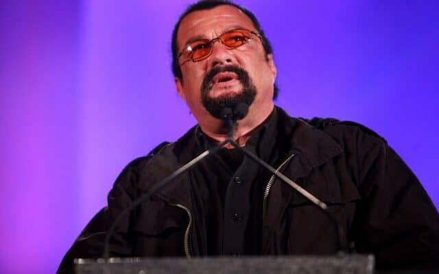 Steven Seagal Speaking at Event Wearing Black Jacket and Orange Sunglasses Wallpaper