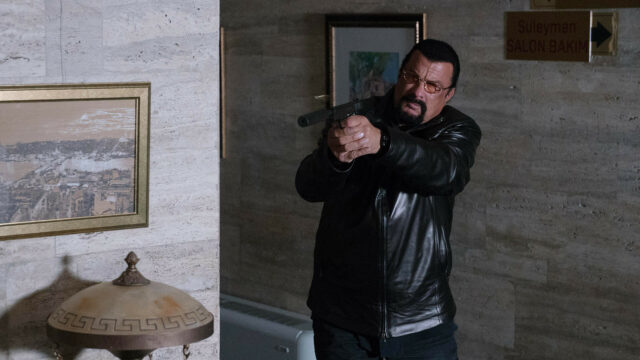 Steven Seagal action pose in black leather jacket holding a gun indoor scene wallpaper