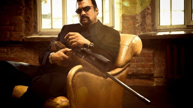 Steven Seagal holding sniper rifle sitting in leather chair stylish action wallpaper