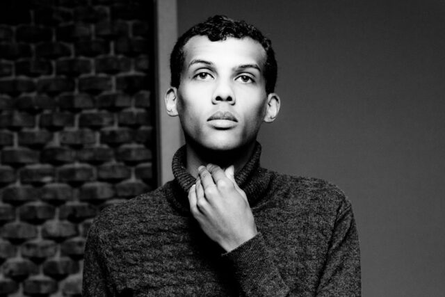 Stromae Black and White Portrait Wallpaper with Moody Expression and Turtleneck Sweater