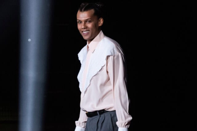Stromae Smiling in Stylish Outfit on Dark Background Wallpaper