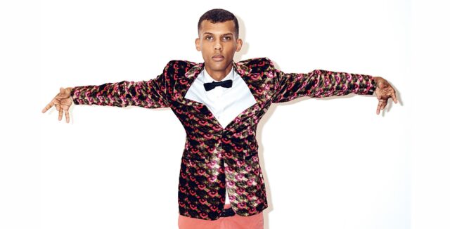 Stromae Stylish Pose in Colorful Patterned Jacket Wallpaper