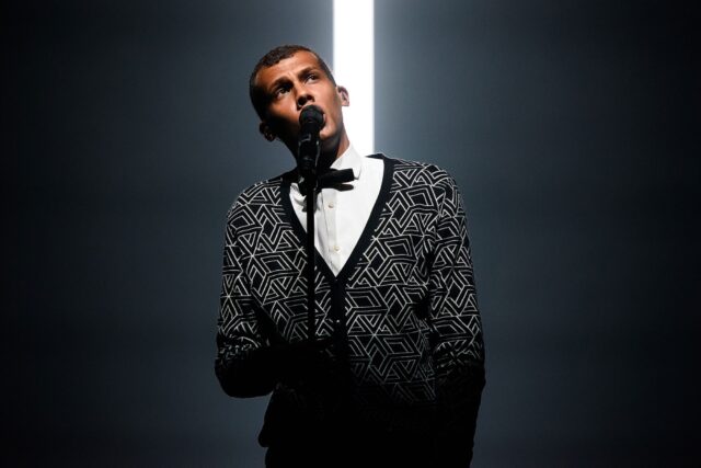 Stromae Wallpapers Stunning Performance with Dramatic Lighting and Geometric Sweater