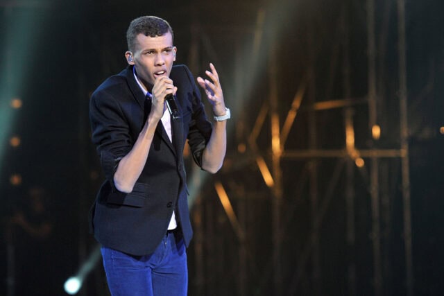 Stromae live performance wallpaper with singer on stage under spotlight