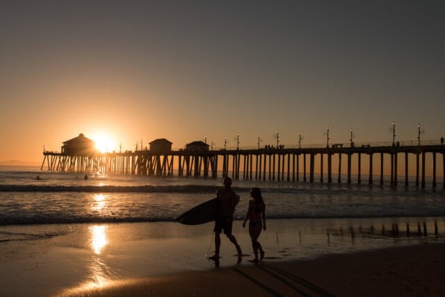 Sunset at Huntington Beach Pier with Surfers Walking on Shoreline Wallpaper