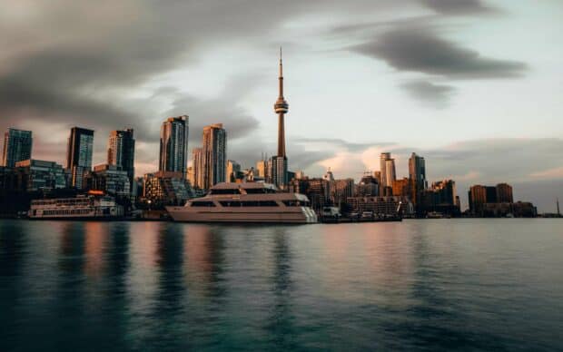 The CN Tower Canada stands tall above the city skyline at sunset with calm water reflections, 2K Desktop Wallpaper