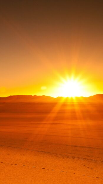 The sun sets behind distant mountains in the Algeria desert, casting long shadows on the sand, 4K Phone Wallpaper