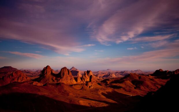 The image shows a stunning sunset casting warm light over rocky mountains in Algeria with a dramatic sky, HD Desktop Wallpaper