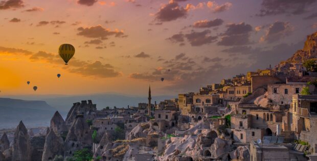 The Cappadocia area with rocky formations and hot air balloons at sunset is shown in this Cappadocia Wallpapers, 2K Desktop Wallpaper