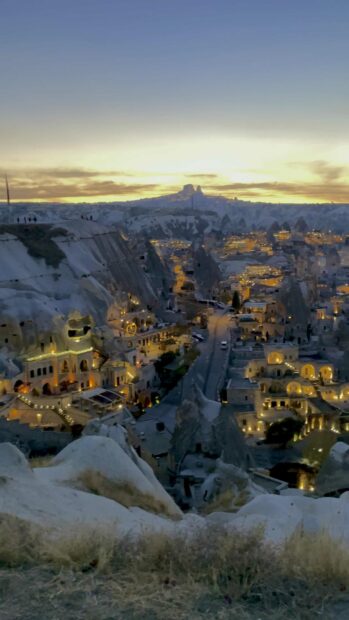 The image shows the illuminated unique rock formations and buildings in Cappadocia during sunset, 4K Mobile Wallpaper