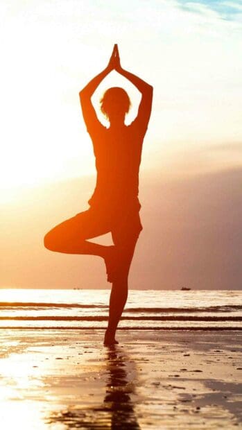 A person practices a yoga pose balancing on one foot by the ocean at sunset, 2K Mobile Wallpaper