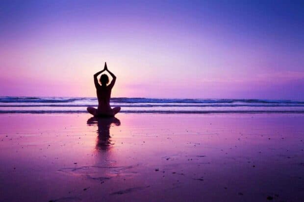 A person practicing yoga in a meditative pose on the beach during sunset with calm ocean waves, 2K Desktop Wallpaper