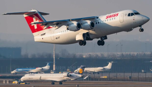A Swiss Avro airplane is captured mid air during takeoff at the airport with other planes in the background, HD Desktop Wallpaper