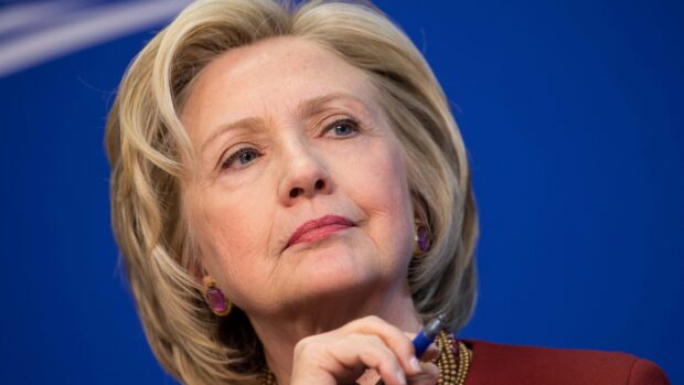 Hillary Clinton is shown with a pensive expression holding a pen, 4K Desktop Wallpaper