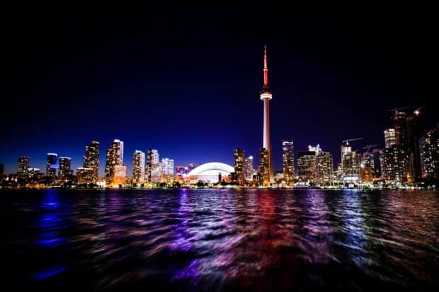 The CN Tower in Canada stands tall above the illuminated city skyline reflected on the water at night
