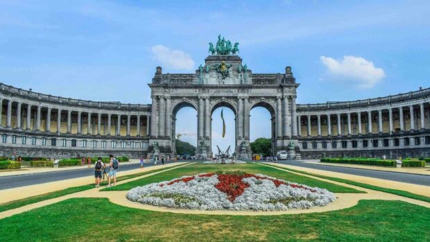 The Triumphal Arch stands in a large garden with flowers and people visiting in Brussels, HD Desktop Wallpaper