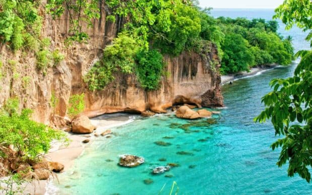 A beautiful tropical coast features cliffs, turquoise water, and greenery in Dominica, 2K Desktop Wallpaper