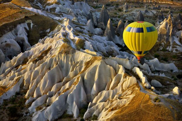 A yellow hot air balloon floats over the unique rock formations of Cappadocia, HD Desktop Wallpaper