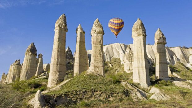 A colorful hot air balloon floats above the unique rock formations in Cappadocia under a clear blue sky, HD Desktop Wallpaper
