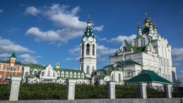 A white cathedral with green roofs and golden domes stands against a blue sky with clouds, 2K Desktop Wallpaper
