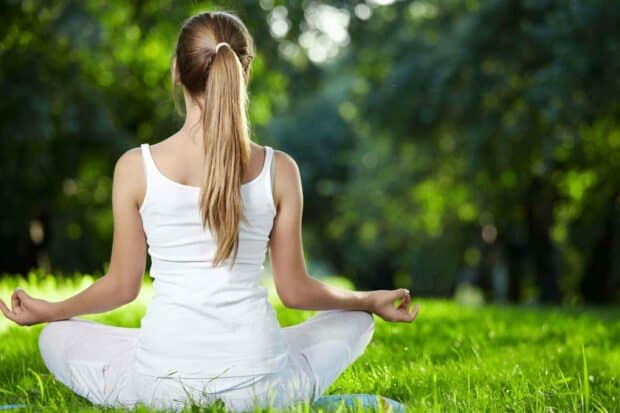 A woman practices yoga sitting cross legged on grass in a tranquil outdoor setting, 2K Desktop Wallpaper