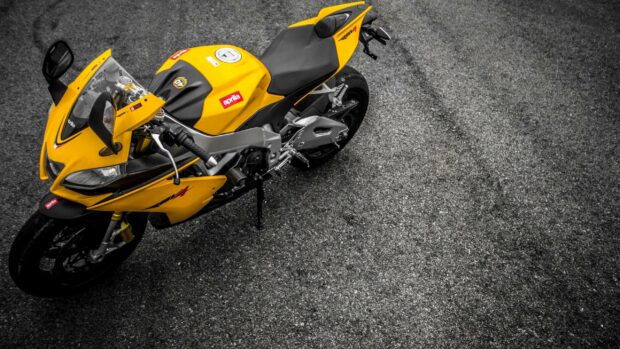 A yellow Aprilia motorcycle is parked on a textured asphalt surface, 2K Desktop Wallpaper