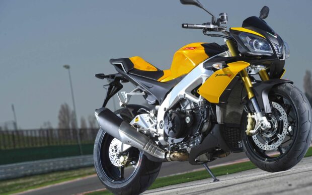 The yellow Aprilia motorcycle is parked on a racing track with a clear sky in the background, 2K Desktop Wallpaper