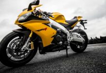 A yellow Aprilia motorcycle is parked on an empty road under a cloudy sky, 2K Desktop Wallpaper
