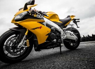 A yellow Aprilia motorcycle is parked on an empty road under a cloudy sky, 2K Desktop Wallpaper