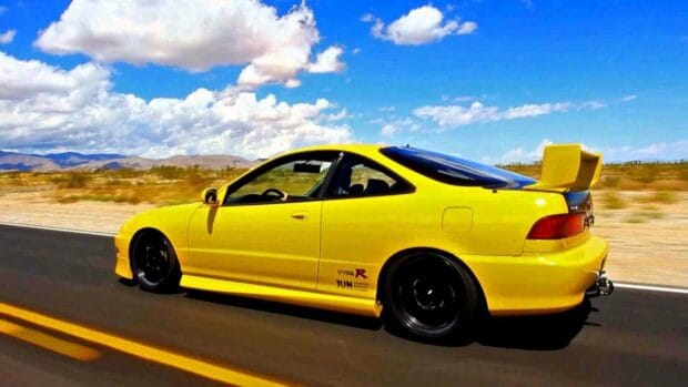 A yellow Honda Integra is speeding down a clear desert highway under a blue sky with clouds, HD Desktop Wallpaper