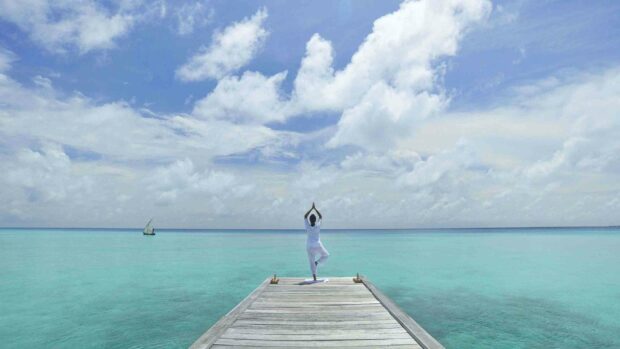 A person is practicing yoga on a wooden dock by the turquoise ocean under a partly cloudy sky, 2K Desktop Wallpaper
