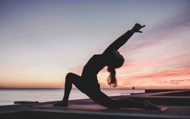 A person practices yoga in a low lunge pose with an extended arm during sunset by the ocean, 2K Desktop Wallpaper