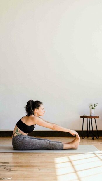 A woman is practicing yoga stretching while seated on a mat in a peaceful room, HD Mobile Wallpaper