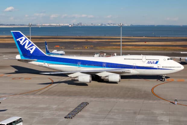 A large ANA aircraft is parked on the tarmac near the sea with service vehicles nearby, HD Desktop Wallpaper