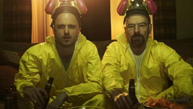 Aaron Paul and another man wear yellow protective suits and helmets while sitting on a couch with drinks, 4K Desktop Wallpaper
