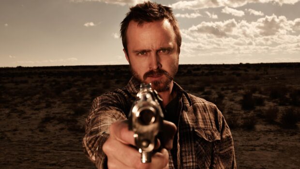 Aaron Paul wallpapers shows him aiming a handgun with a serious expression in a barren desert, 4K Desktop Wallpaper