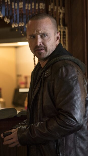 Aaron Paul wears a brown leather jacket and looks concerned indoors, 2K Mobile Wallpaper
