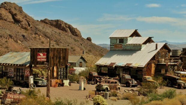 An old ghost town with vintage cars and weathered buildings in a desert landscape, 4K Desktop Wallpaper