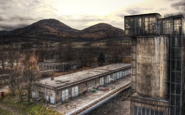 A view of old industrial buildings with overgrown vegetation in a ghost town landscape, 2K Desktop Wallpaper