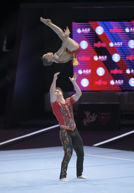 A male athlete is throwing a female gymnast in a toss during an acrobatic gymnastics performance, 2K Desktop Wallpaper