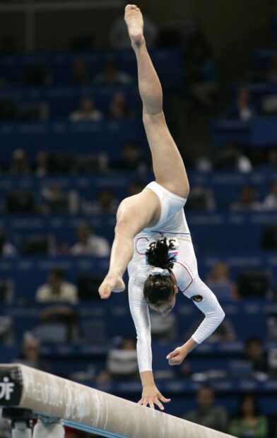A gymnast is balancing in a handstand pose on the beam during a competition involving acrobatic gymnastics, HD Mobile Wallpaper